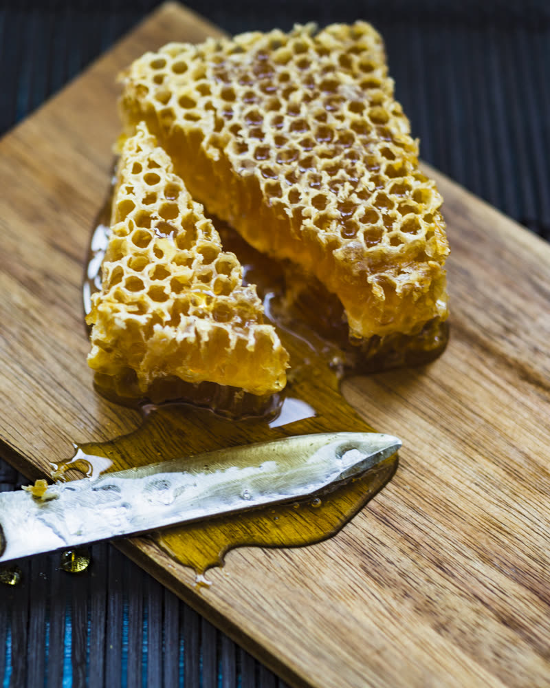 Pedaços de favo de mel sobre tábua de madeira, ao lado de uma faca